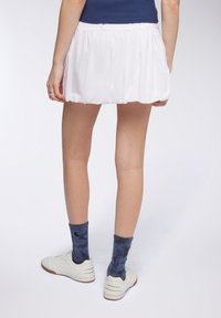 Gonna bianca a pieghe con vita elastica, abbinata a calzini a righe navy e sneakers bianche. Focus sulla texture del tessuto e sui dettagli del design.