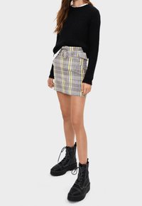 Černý pletený svetr, kostkovaná mini sukně s žlutými akcenty a páskem, doplněná černými kordovými bojovými botami s tlustou podešví.