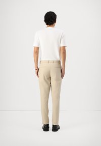 Beige kalhoty s elastickým pasem, kombinované s bílou košilí s krátkým rukávem; zobrazeno zezadu na jednobarevném pozadí.