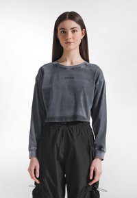Sudadera gris recortada con mangas largas, con cuello redondo y la palabra "DEHA" impresa en el frente. Combinada con pantalones negros con cordón ajustable.