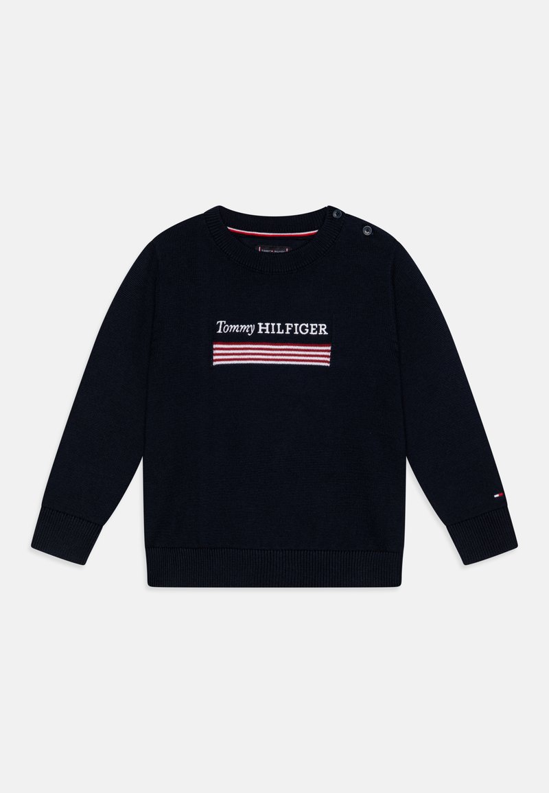 Tumši zilā džemperis ar garām piedurknēm, apaļu dekoltē, ribotām piedurkņu un apakšdaļas malām. Iezīmēts ar izšūtu "Tommy HILFIGER" logotipu ar sarkaniem un baltajiem svītrām.