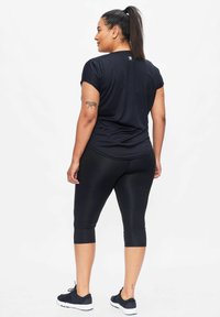 Zwarte sportieve shirt met korte mouwen, gecombineerd met zwarte capri leggings en zwarte sneakers. Glad materiaal met een nauwsluitend ontwerp, zichtbaar logo op het shirt.