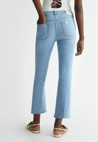 Jasnoniebieskie dżinsy dzwony z tylnymi kieszeniami i średnim stanem. Tkanina wydaje się gładka z lekkim streczem.