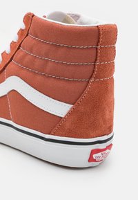 Vysoké tenisky v spálenej oranžovej plátne s nubukovými detailami. Biely bočný pruh a šitie, čierna gumená podrážka a červené logo na päte.