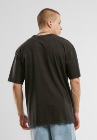 Fekete, oversize pamut póló, rövid ujjakkal és kerek nyakkivágással, nyers szélű aljjal és finom textúrával.