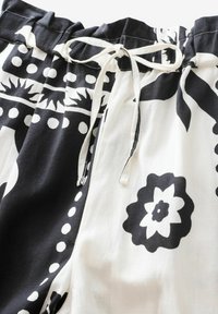 Pantalones a rayas en blanco y negro con cintura ajustable, que presentan diseños florales y lunares sobre una tela texturizada.