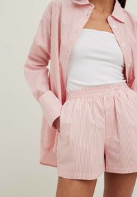 Randig skjorta i rosa och vitt av bomull med matchande shorts med elastisk midja. Skjortan har långa ärmar och en avslappnad passform.