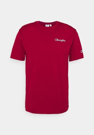T-shirt en coton rouge à manches courtes, col rond, avec le logo "Champion" brodé sur la poitrine et la manche. Texture lisse.