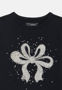 Camiseta negra con un diseño de lazo blanco texturizado y brillante, acompañado de estrellas plateadas dispersas. La etiqueta dice "FRIBOO," tamaño 7/8 (27/28).