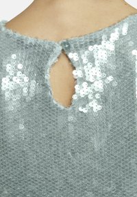 Lichtgrijze gebreide top met een sleutelgatopening op de rug, versierd met zilverkleurige pailletten in een verspreid patroon, met een knoopsluiting.