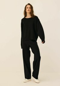 Czarny, oversize sweatshirt z wytłoczonym napisem "ATHLETICS" na piersi, zestawiony z luźnymi czarnymi spodniami i białymi trampkami.