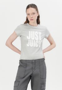 Siva majica s kratkim rukavima s velikim bijelim natpisom "JUST JUICY", u kombinaciji sa sivim cargo hlačama s džepovima i vidljivim šavovima.