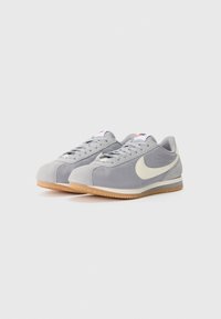 Gray suede sneakers with a white Nike swoosh, flat laces, and gum rubber outsole. Features a low-profile design and rounded toe shape.