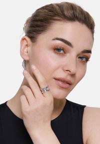 Anello d'argento con design intrecciato, caratterizzato da superfici lucide e testurizzate. Indossato su un dito, mette in evidenza i dettagli e l'artigianato.