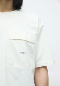 Lysfarget bomull T-skjorte med brystlomme og trykt "OAKLEY F.G.L."-logo, korte ermer og avslappet passform.