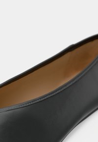Scarpa piatta nera in pelle con una texture liscia e punta arrotondata. All'interno presenta una fodera beige, creando un contrasto con il colore esterno.