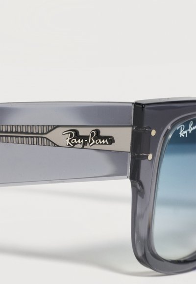 Крупен план на сив прозрачен ръкав на слънчеви очила Ray-Ban със сребристо лого Ray-Ban и сини оттенъци на лещите на бял фон.