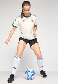White shirt with green accents, black shorts, white socks with blue stripes, and black cleats. A blue and white soccer ball is on the ground.