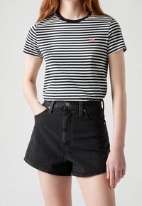 Czarna i biała koszulka w paski z krótkim rękawem, prążkowany okrągły dekolt oraz małe czerwone logo na piersi, w zestawieniu z szortami z czarnego denimu o wysokim stanie.