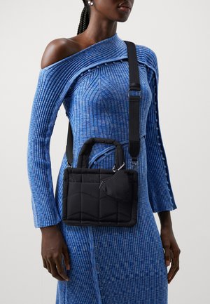 Zwarte gewatteerde handtas met korte handvatten en een verstelbare band, voorzien van een klein vak met ritssluiting. Draagt over een textuurblauwe jurk.