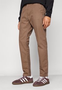 Bruna bomullschinos med en texturerad yta, utrustad med sidofickor. Tillsammans med mörklila sneakers och vita detaljer på skorna.