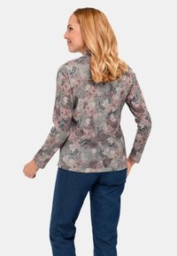 Langarmshirt aus gemustertem Stoff mit Wirbel aus Grau, Rosa und Creme. Kombiniert mit dunkelblauen Hosen; lockere Passform. Rückansicht sichtbar.