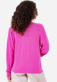 Pull rose vif à coupe ample, manches longues et poignets côtelés. Texture lisse et détails minimalistes, vu de dos.