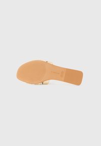 Suela de sandalia beige con un fondo de goma texturizada, parte superior de cuero suave y un acento de tira metálica. Ligera y con forma redondeada.