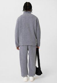Grijze fleece pullover en bijpassende broek met een gestructureerde afwerking. Losse pasvorm, lange mouwen, achterzakken en witte sneakers. Zwarte crossbody tas.