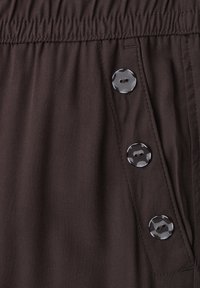 Dark brown fabric with elastic waistband and three shiny black buttons arranged vertically next to a slanted pocket opening.