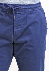 Námořnické modré kalhoty na stažení vyrobené z měkké látky, mají hladký povrch, elastický pas a boční kapsy.