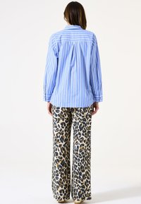 Camisa a rayas en azul y blanco con puños abotonados, combinada con pantalones de pierna ancha que presentan un estampado de leopardo en beige y negro.