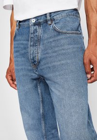 Light blue denim jeans featuring a classic straight cut, five-pocket design, and contrasting stitching. Button closure and belt loops included.
