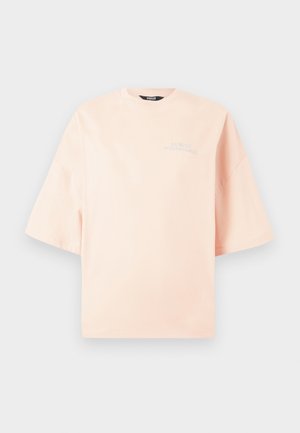 Rózsaszín, túlságosan nagy póló, puha pamutból készült. Rövid ujjú és kerek nyakú, bal oldalon hímzett logóval.