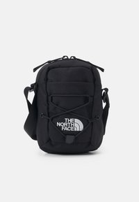 Borsa a tracolla nera in tessuto con chiusura zip, cordini frontali in bungee e un logo bianco ben visibile sul pannello frontale inferiore.