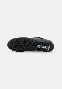 Svart såle av sneakers med teksturert gummi for grep, med et merke-logo og modellnavn i hvitt på siden, designet for holdbarhet.
