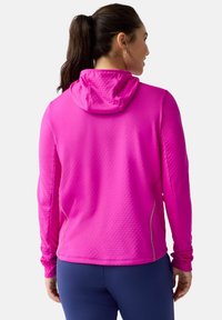 Felpa con cappuccio rosa brillante in tessuto texturizzato, con maniche lunghe e cuciture piatte. Presenta un design aderente e una tasca laterale con zip.