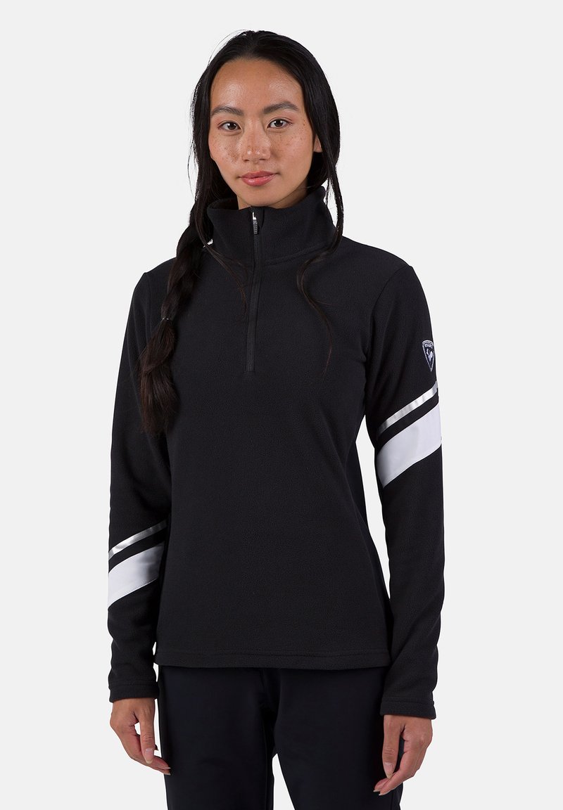 Svart fleecepullover med hög krage, prydd med silver- och vita ränder på armarna och dragkedja i halsen. Mjuk, strukturerad yta.