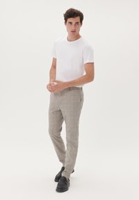 Weißes T-Shirt mit Rundhalsausschnitt, kombiniert mit hellgrauen karierten Hosen und schwarzen Loafers, die ein dezentes orangefarbenes Muster im Stoff aufweisen.