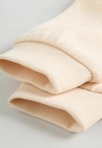 Tela de algodón beige con puños acanalados, que muestra una textura suave y un acabado limpio. Dos mangas dobladas posicionadas juntas sobre una superficie plana.