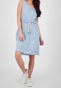 Vestido sin mangas a rayas azules con cintura elástica, cordón y un pequeño logo en forma de corazón. Se lleva con zapatillas blancas sobre un fondo neutro.