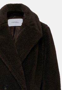 Cappotto fluffoso di un marrone scuro con un ampio colletto, chiusura a bottoni e una fodera liscia. L'etichetta riporta "COMMA". Il tessuto strutturato aggiunge profondità.