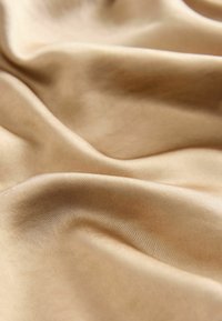 Tela de satén en un suave tono beige, con una textura lisa y un ligero brillo, drapeada en suaves pliegues que crean una apariencia fluida.