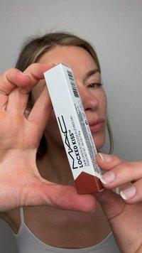 Frau hält eine MAC Locked Kiss 24-Stunden Lippen- und Haarlippenstiftbox nah an der Kamera vor einem einfarbigen Hintergrund.