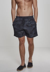 Schwarze Camouflage-Badehosen mit einem elastischen Bund und Kordelzug, aus einem glatten, leichten Stoff und mit zwei seitlichen Taschen.