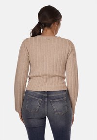 Maglione beige a coste con maniche lunghe, design aderente, motivo a maglia testurizzata e scollatura tonda, abbinato a jeans blu scuro.