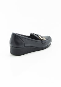 Zapato de cuero negro con un tacón bajo, que presenta una correa texturizada y un detalle de hebilla dorada. Punta redondeada y acabado suave. Se muestra en vista lateral.