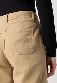 Kaki bukser med baglommer, lavet af tekstureret stof. Designet har en høj talje og en afslappet pasform, accentueret af sydde sømme.
