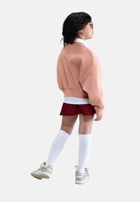 Sudadera rosa de gran tamaño, camisa blanca de cuello debajo, falda roja, medias blancas hasta la rodilla y zapatillas beige con detalles.