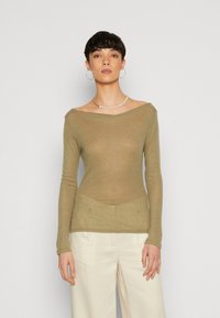 Olivengrønn langermet topp med off-shoulder hals og teksturert stoff, sammen med kremfargede vide bukser.